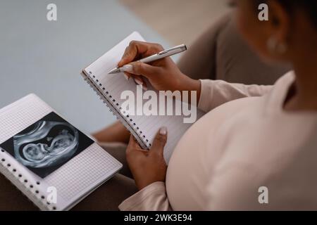 Hochwinkelansicht einer schwarzen Schwangeren, die Notizen macht Stockfoto