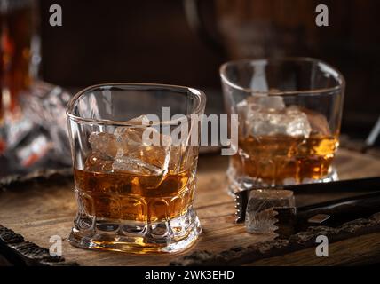 Zwei Gläser Whiskey mit Eis auf rustikalem Holztablett mit Dekanter im Hintergrund Stockfoto