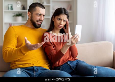 Ein gestresstes junges Paar, das zu Hause auf der Couch auf das Smartphone blickt Stockfoto