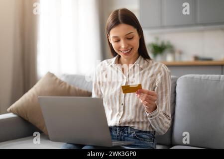 Glückliche junge Frau mit Kreditkarte und Laptop auf dem Sofa Stockfoto