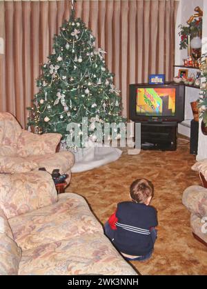 1990er Jahre dreijähriger Junge historisches Archiv Rückansicht Bild Fernsehen altmodischer Farbfernseher neben dekoriertem Weihnachtsbaum auf Teppich in 90er Jahre möbliertem Haus Wohnzimmer mit Vorhängen gezeichnet Essex England UK Stockfoto