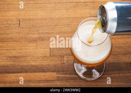 Craft Beer wird aus einer Dose in ein Glas gegossen, das auf einem Holztisch in warmen Farben steht Stockfoto