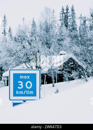 Dieses Bild zeigt eine ruhige Winterszene, in der ein blaues Geschwindigkeitsbegrenzungsschild mit einer maximalen Geschwindigkeit von 30 km/tim in scharfem Kontrast zur weißen Schneedecke steht Stockfoto