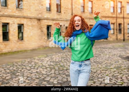 Eine entzückte junge rothaarige Frau im Urlaub. Ein Tourist mit Rucksack, gekleidet in einem grünen Pullover, der im Urlaub durch eine alte europäische Stadt spaziert. Stockfoto
