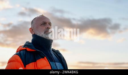 Porträt eines Reifen alten Mannes, der an einem kalten sonnigen Tag in den Bergen vor dramatischem Himmelhintergrund wandert. Freiraum, Freiheit, Bewegung und Fitness für Stockfoto