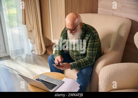 Der grauhaarige alte Mann arbeitet mit Dokumenten im Wohnzimmer Stockfoto