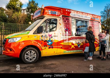 Leute kaufen Eis aus einem elektrisch betriebenen Eiswagen an einem sonnigen Winternachmittag. Umweltfreundlich, Elektrofahrzeug, Anbieter, Wales, Cardiff. Stockfoto