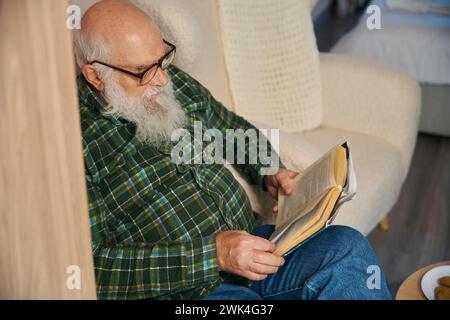 Ein alter Mann in einem warmen karierten Hemd liest ein Buch Stockfoto