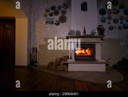 Geschlossener Kamin mit Holzofen im Kamin, Keramikplatten an der Wand und Holzboden im Zimmer Stockfoto