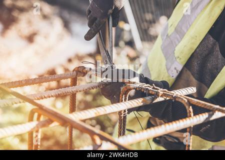 Ein Arbeiter verwendet Stahlbindedraht, um Stahlstäbe in Nahaufnahme an Verstärkungsstäben zu befestigen. Stahlbetonkonstruktionen - Herstellung eines Stahlverstärkungskäfigs f Stockfoto