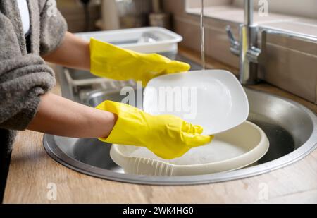 Frau in gelben Handschuhen, die Geschirr in der Küche waschen. Seitenansicht einer hübschen jungen Hausfrau, die Haushalt macht. Waschplatten mit Innengewinde Stockfoto