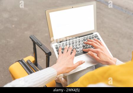 Glückliche Frau am Bahnhof, die auf einen Zug wartet und am Computer arbeitet. Stockfoto