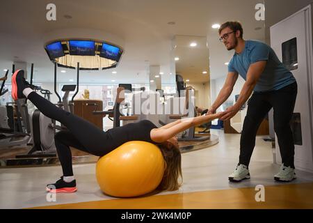 Der Trainer hilft einer Frau, Übungen auf einem gelben Fitball durchzuführen Stockfoto