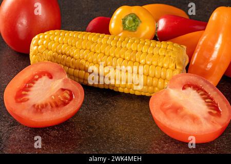 Nahaufnahme eines tiefen Fotos einer lebendigen Gemüsemischung mit Reifen roten Tomaten, farbenfrohen Paprika und goldenen Maiskernen, die einem dramatischen Schauspiel gegenüberstehen Stockfoto