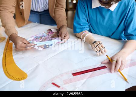 Hochwinkelnaht eines nicht erkennbaren Mädchens mit Armprothetik, das an Kleidungsmustern im inklusiven Atelier-Kopierraum arbeitet Stockfoto