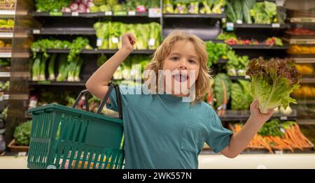 Kind mit Salatsalat. Lustiges, süßes Kind beim Einkaufen im Supermarkt. Lebensmittelgeschäft. Lebensmittelladen, gesundes Lifestyle-Konzept. Stockfoto