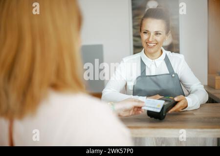 40 Jahre alter Friseurangestellter in modernem Schönheitsstudio, der Kunde akzeptiert Kreditkartenzahlungen über das Terminal an der Rezeption. Stockfoto