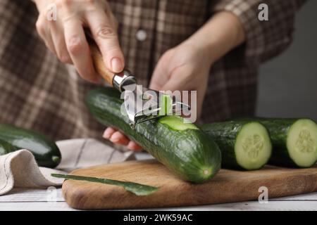 Frau, die frische Gurke am weißen Holztisch schält, Nahaufnahme Stockfoto