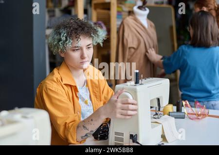Porträt eines tätowierten Teenagermädchens, das Nähmaschinen im Kopierraum der Schneiderwerkstatt aufstellt Stockfoto