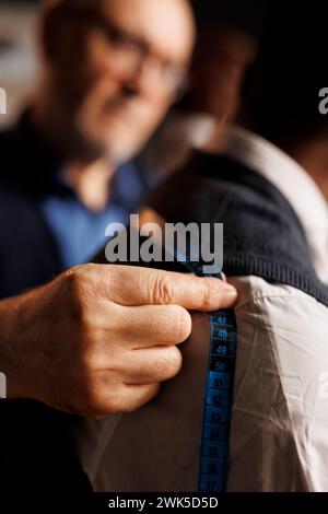 Fachkundiger, präziser Handwerker, der Passmaße am Sartorialstück mit Klebeband annimmt. Präziser, erfahrener Schneider hilft Kunden mit maßgeschneiderten, stilvollen Anzügen aus nächster Nähe Stockfoto