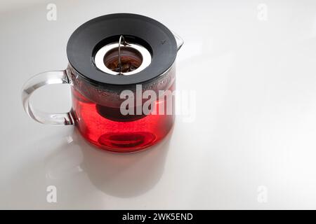 Eine Teekanne aus Glas mit einem Fruchtaufguss, Infuser-Krug mit Erdbeeraufguss, roter Tee, Apfelaufguss auf einem weißen Tisch, Kopierraum, horizontal Stockfoto