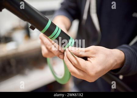 Unerkennbare Person, die einen Fahrradrahmen mit Abdeckband für ein individuelles Maldesign in seiner Fahrradwerkstatt vorbereitet, ein handgefertigter kreativer Prozess. Stockfoto