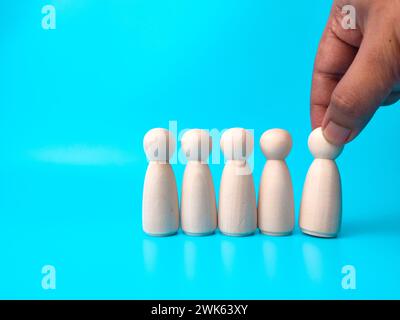 Hand mit einer von fünf Holzfiguren auf blauem Hintergrund. Wahlkonzept. Stockfoto