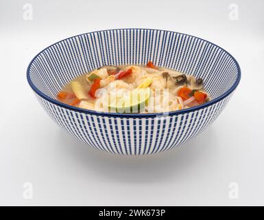 Eine Profilperspektive zeigt japanische Ramen-Nudelsuppe, geschmückt mit Garnelen, Pilzen, Tomaten, Zitronengras, und Limette, serviert in klassischem Blau Stockfoto