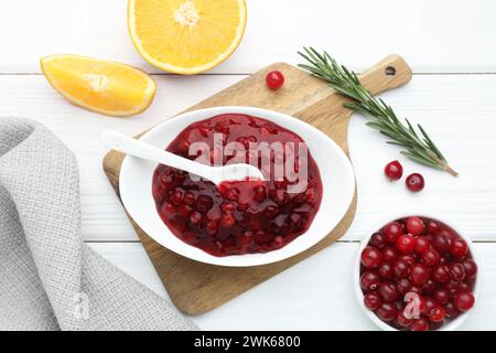 Leckere Preiselbeersoße in Schüssel, frische Beeren, Orangenscheiben und Rosmarin auf weißem Holztisch, flach gelegt Stockfoto