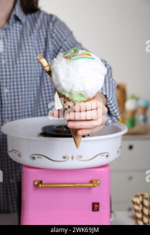 Frau mit Waffelkegel und Zuckerwatte in der Nähe der Maschine, Nahaufnahme. Nachtisch machen Stockfoto