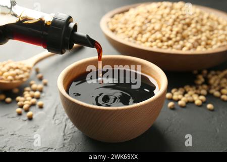 Leckere Sojasauce aus der Flasche in die Schüssel auf dem schwarzen Tisch gießen, Nahaufnahme Stockfoto