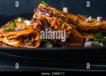 3 Rindfleisch Birria Tacos auf schwarzer Platte gestapelt Stockfoto