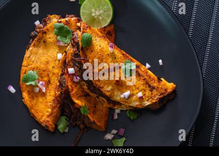 3 Rindfleisch Birria Tacos auf schwarzer Platte gestapelt Stockfoto