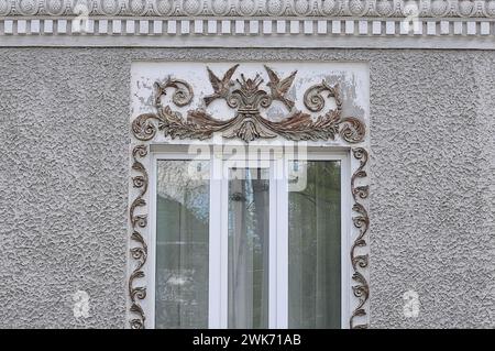 Das Fenster des Häuschens ist mit Mustern von Pflanzen und Vögeln dekoriert, Stuckdekoration auf der Fassade Stockfoto