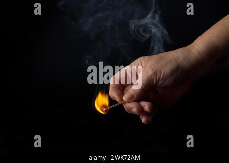 Nahaufnahme einer Frauenhand, die ein Streichholz auf schwarzem Hintergrund anzündet Stockfoto