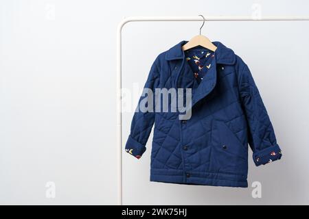 Blauer gesteppter Kindermantel am Aufhänger an der weißen Wand Stockfoto