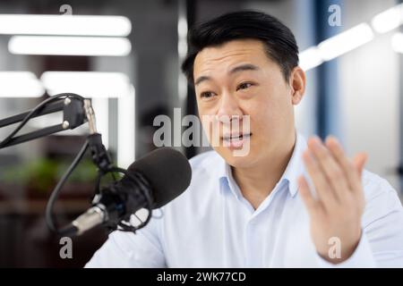Nahaufnahme eines asiatischen jungen Mannes, der im Büro an einem Schreibtisch vor einem Mikrofon sitzt und ein Online-Meeting per Videoanruf abhält, diskutiert, erklärt, mit der Hand Gesten gibt. Stockfoto