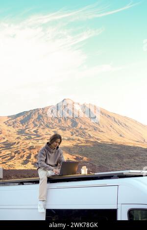 Mann sitzt auf einem Dach mit einem Laptop vor einer majestätischen Berglandschaft. Stockfoto