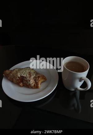 Frisch gebackenes köstliches Brötchen mit Käse auf einem Teller und eine Tasse Kaffee mit Milch. Leckeres Frühstück Stockfoto