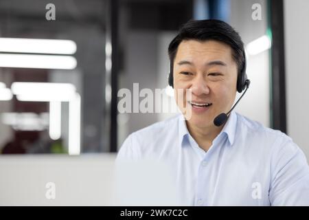 Mann mit Headset-Telefon-Nahaufnahme am Arbeitsplatz im Büro, Asiatisch in Hemd Kundendienstmitarbeiter, Geschäftsmann, der Laptop für Videoanrufe benutzt, und Kundenberatung, Telefonverkauf, Stockfoto