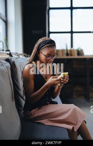 Porträt einer schönen Frau, die in einem modernen Büro sitzt und auf das Smartphone schaut, während sie eine Pause macht. Arbeiten aus der Ferne vom Café aus, entspannte Atmosphäre Stockfoto