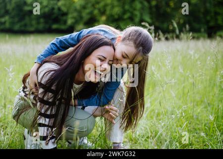 Schöne Mutter mit Tochter, spielt auf der Wiese, Huckepack, hat Spaß. Muttertag und mütterliche Liebe. Stockfoto