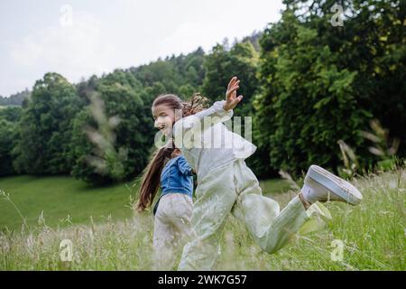 Zwei Schwestern spielen auf der Wiese in hohem Gras, haben Spaß, laufen lachend. Schwesternliebe und Geschwisterbeziehung. Stockfoto