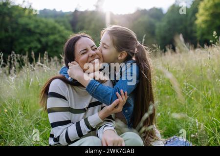 Schöne Mutter mit Tochter, umarmt oder umarmt, sitzt im Gras auf der Wiese. Muttertag und mütterliche Liebe. Stockfoto