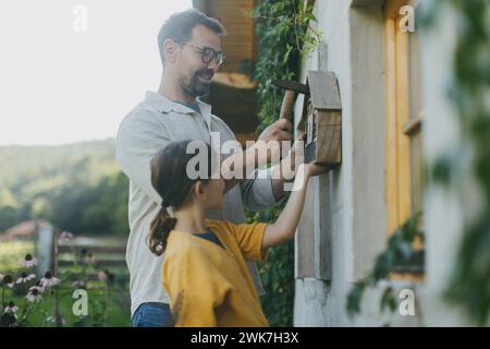 Vater mit Tochter macht ein Insektenhotel oder Insektenhaus draußen im Garten. Mädchen, das über Insekten, Gartenökosystem und Biodiversität lernt. Stockfoto