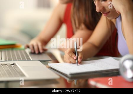 Nahaufnahme zweier Schüler, die online lernen und sich Notizen an einem Schreibtisch machen Stockfoto