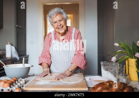 Seniorin, die traditionelle ostermahlzeiten für die Familie zubereitet, Teig für osterbrötchen kneten. Nachbildung von Familienrezepten, individuell. Stockfoto