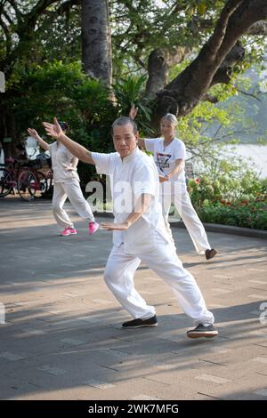 Leute, die am frühen Morgen Tai Chi rund um den Hoan Kiem See in Hanoi, Vietnam, machen Stockfoto