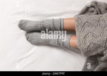 Zwei weibliche Beine tragen kuschelige graue Kaschmirsocken unter der Decke im Bett, Nahaufnahme Stockfoto