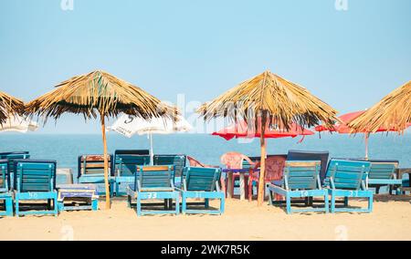 Leere Liegen unter Strohschirmen an einem Sandstrand in Goa Indien. Sonnenschirme mit Palmblättern. Goa Indien Februar-16,2024 Stockfoto